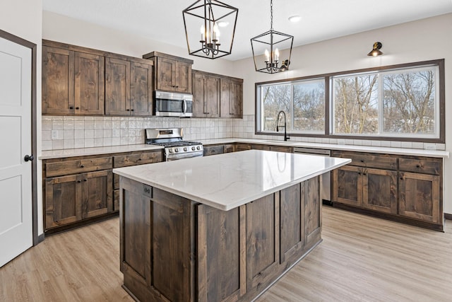 kitchen with appliances with stainless steel finishes, a kitchen island, hanging light fixtures, light hardwood / wood-style floors, and dark brown cabinetry