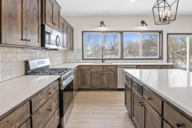 kitchen with tasteful backsplash, sink, light wood-type flooring, stainless steel appliances, and decorative light fixtures