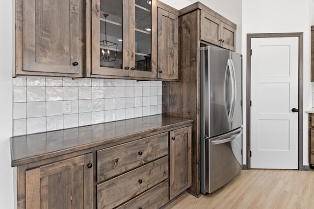 kitchen with backsplash, dark brown cabinets, light wood-type flooring, and stainless steel fridge