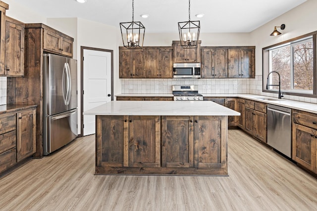 kitchen with appliances with stainless steel finishes, sink, light hardwood / wood-style floors, dark brown cabinetry, and a center island