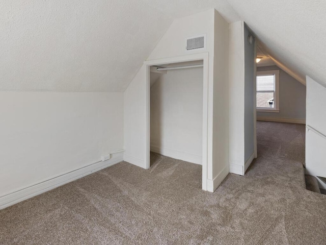 additional living space with a textured ceiling, vaulted ceiling, and dark colored carpet