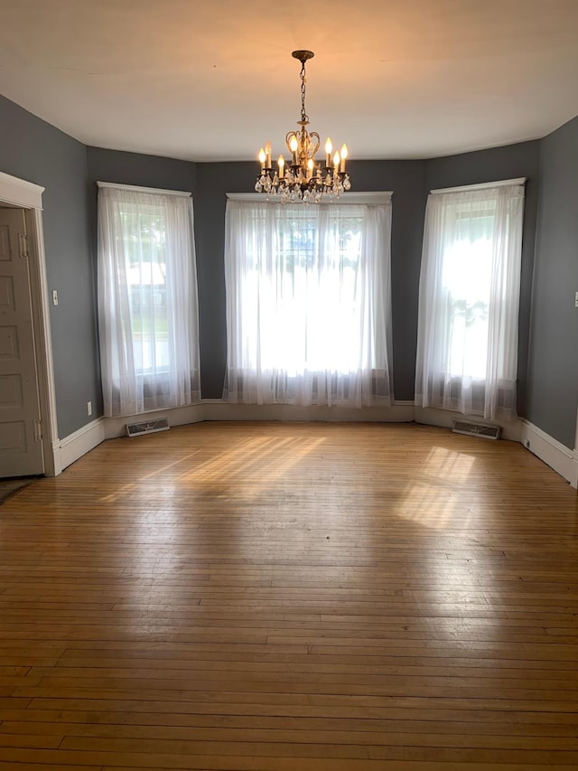 unfurnished dining area with hardwood / wood-style floors and a notable chandelier