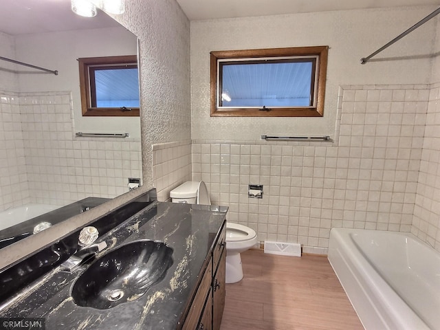 full bathroom featuring toilet, wood-type flooring, tiled shower / bath, vanity, and tile walls