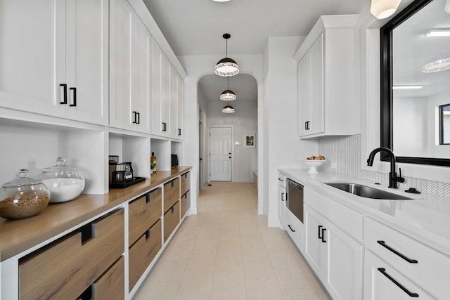 kitchen with sink, white cabinets, light stone counters, and decorative light fixtures