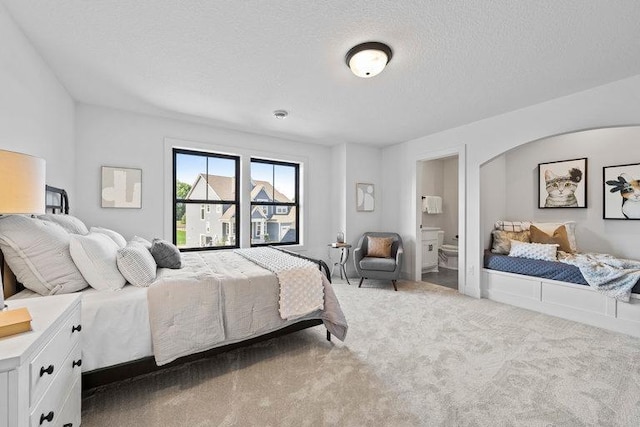 bedroom with a textured ceiling, light carpet, and ensuite bathroom