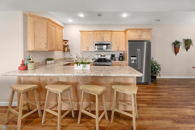 kitchen with stainless steel appliances, sink, kitchen peninsula, light brown cabinetry, and dark hardwood / wood-style floors