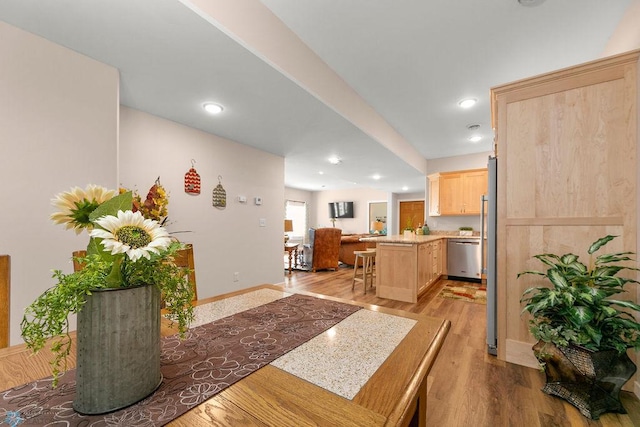 kitchen featuring a center island, light hardwood / wood-style flooring, stainless steel dishwasher, kitchen peninsula, and light brown cabinetry