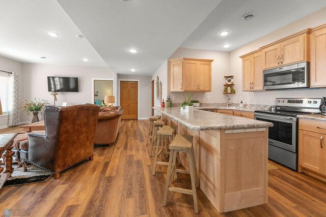 kitchen featuring kitchen peninsula, hardwood / wood-style flooring, stainless steel appliances, a kitchen breakfast bar, and sink