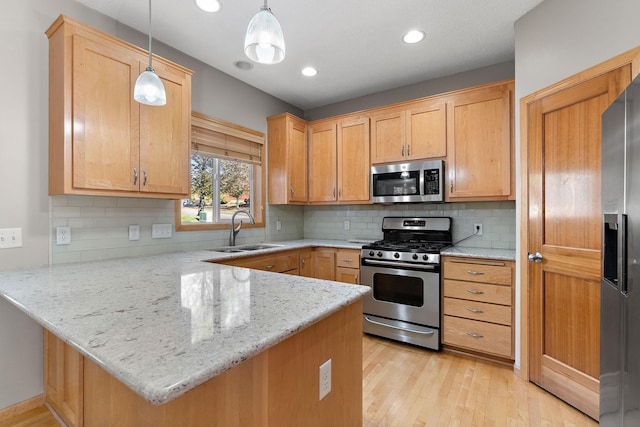 kitchen with stainless steel appliances, pendant lighting, sink, light hardwood / wood-style floors, and kitchen peninsula