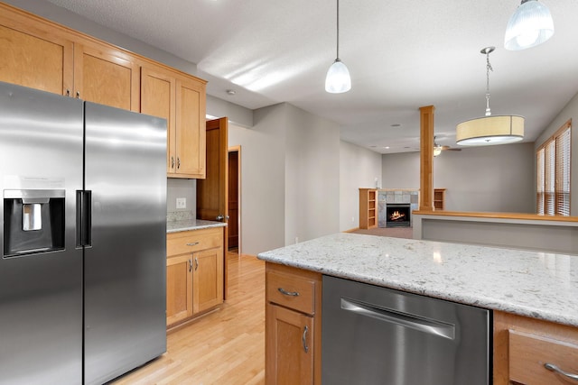 kitchen with stainless steel appliances, light stone counters, light wood-type flooring, a fireplace, and pendant lighting