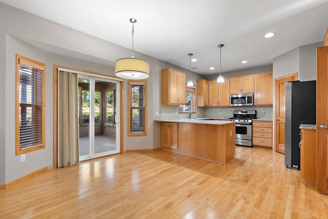 kitchen with sink, appliances with stainless steel finishes, kitchen peninsula, hanging light fixtures, and light hardwood / wood-style flooring