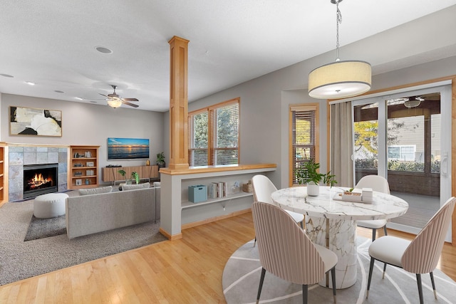 dining area with ceiling fan, a tile fireplace, light wood-type flooring, and a textured ceiling