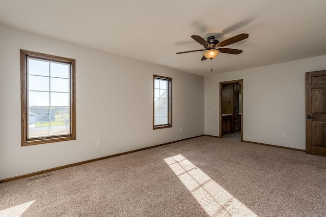 unfurnished bedroom with multiple windows, ensuite bath, light colored carpet, and ceiling fan