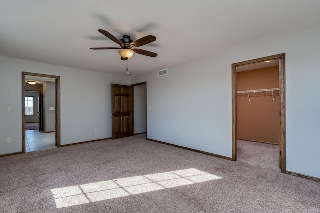 unfurnished bedroom featuring light carpet, a closet, a spacious closet, and ceiling fan