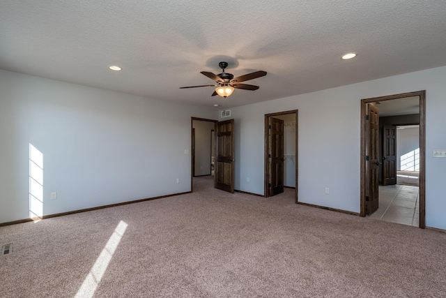 unfurnished bedroom with light carpet, ceiling fan, a textured ceiling, a closet, and a walk in closet