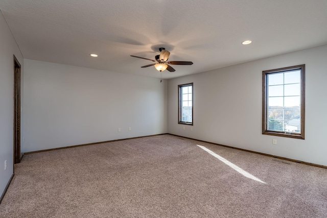 carpeted empty room with ceiling fan, a healthy amount of sunlight, and a textured ceiling