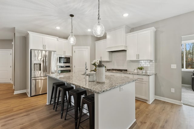 kitchen featuring white cabinets, stainless steel appliances, light wood-type flooring, and an island with sink