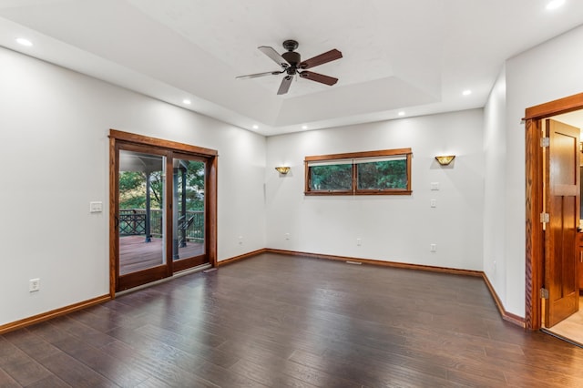 unfurnished room featuring dark hardwood / wood-style flooring, a tray ceiling, and ceiling fan