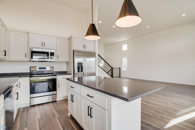 kitchen with a kitchen island, stainless steel appliances, hardwood / wood-style floors, decorative light fixtures, and white cabinetry