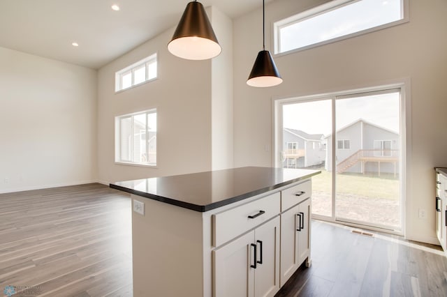 kitchen with wood-type flooring, a kitchen island, hanging light fixtures, a high ceiling, and white cabinets