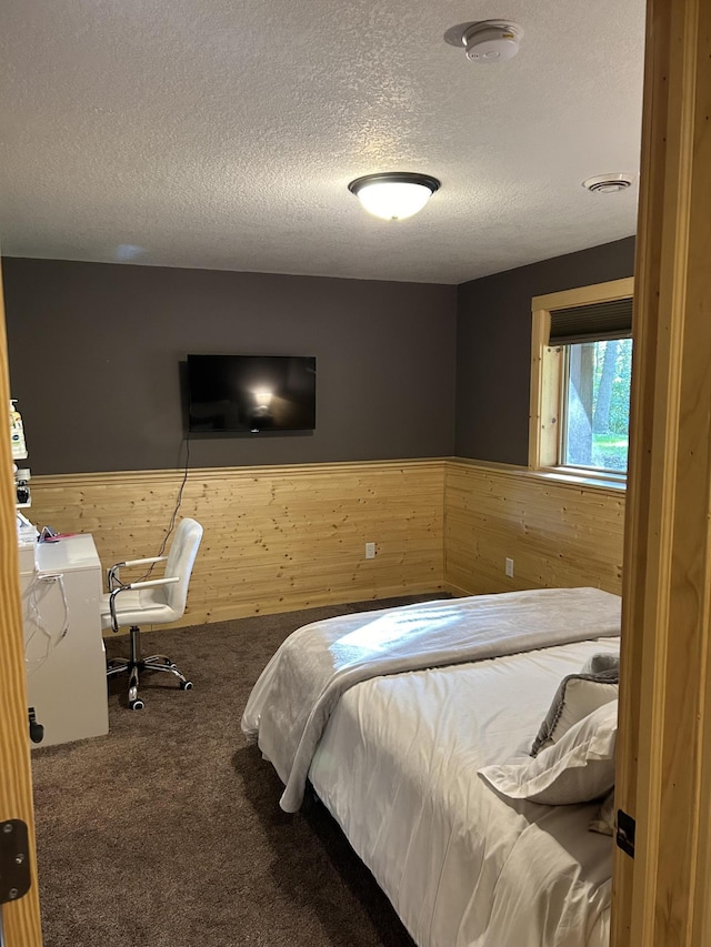 bedroom with carpet, a textured ceiling, and wooden walls