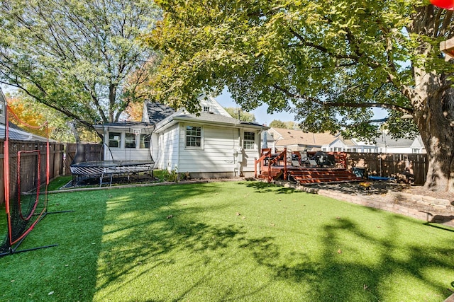 rear view of house with a yard, a trampoline, and a wooden deck