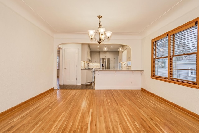 unfurnished living room with sink, light hardwood / wood-style flooring, and an inviting chandelier