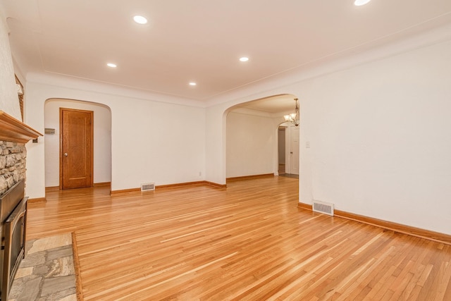 unfurnished living room featuring light hardwood / wood-style floors, a stone fireplace, crown molding, and an inviting chandelier