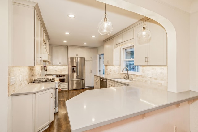 kitchen featuring kitchen peninsula, appliances with stainless steel finishes, dark wood-type flooring, sink, and decorative light fixtures