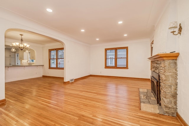 unfurnished living room featuring a stone fireplace, sink, crown molding, light hardwood / wood-style floors, and a chandelier