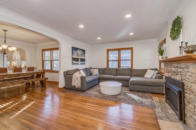 living room featuring a stone fireplace, a healthy amount of sunlight, wood-type flooring, and a notable chandelier