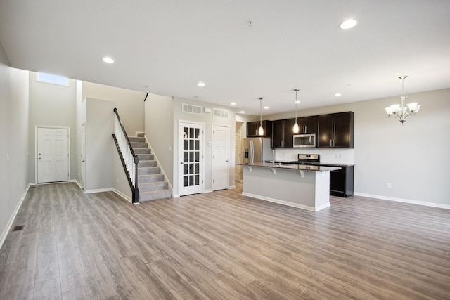 kitchen featuring an island with sink, hanging light fixtures, stainless steel appliances, and light hardwood / wood-style floors