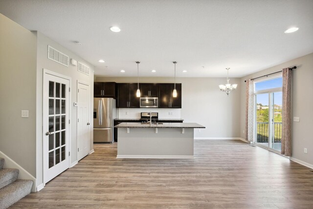 kitchen with appliances with stainless steel finishes, sink, light wood-type flooring, decorative light fixtures, and a center island with sink