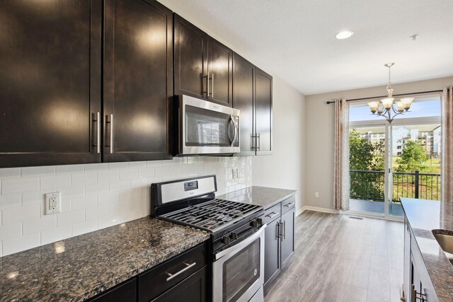 kitchen featuring decorative backsplash, appliances with stainless steel finishes, light wood-type flooring, and dark stone countertops