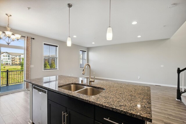 kitchen featuring light hardwood / wood-style flooring, a center island with sink, sink, an inviting chandelier, and stone counters