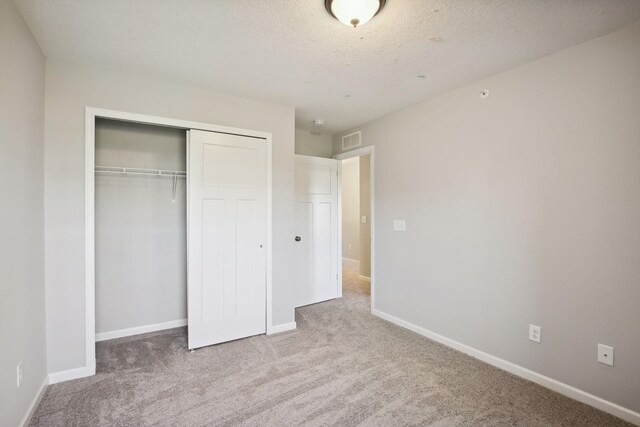 unfurnished bedroom featuring a textured ceiling, light colored carpet, and a closet