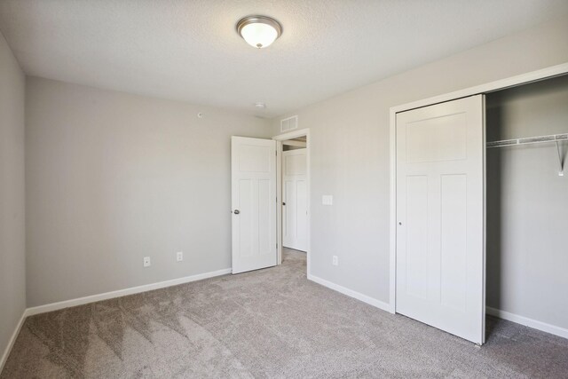 unfurnished bedroom featuring a closet, a textured ceiling, and light colored carpet