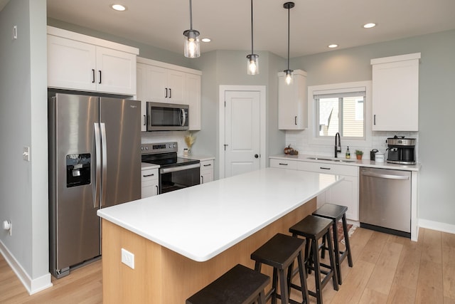 kitchen with a kitchen island, appliances with stainless steel finishes, white cabinetry, light hardwood / wood-style floors, and sink