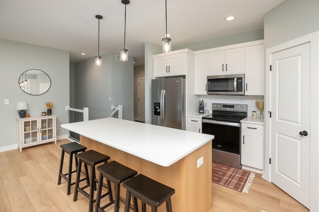 kitchen with a kitchen island, appliances with stainless steel finishes, light hardwood / wood-style flooring, and white cabinetry