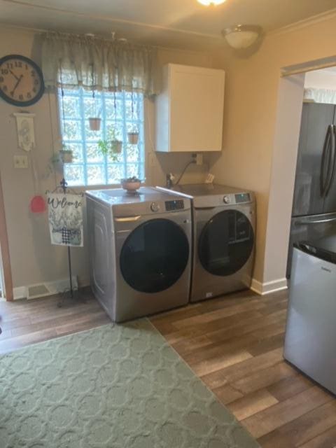 clothes washing area with washer and dryer, hardwood / wood-style flooring, crown molding, and cabinets