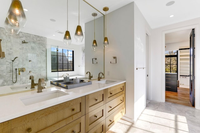 bathroom with tile patterned flooring, tiled shower, vanity, and a healthy amount of sunlight