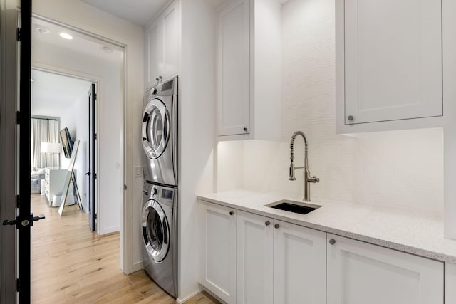 washroom featuring stacked washing maching and dryer, cabinets, light hardwood / wood-style floors, and sink