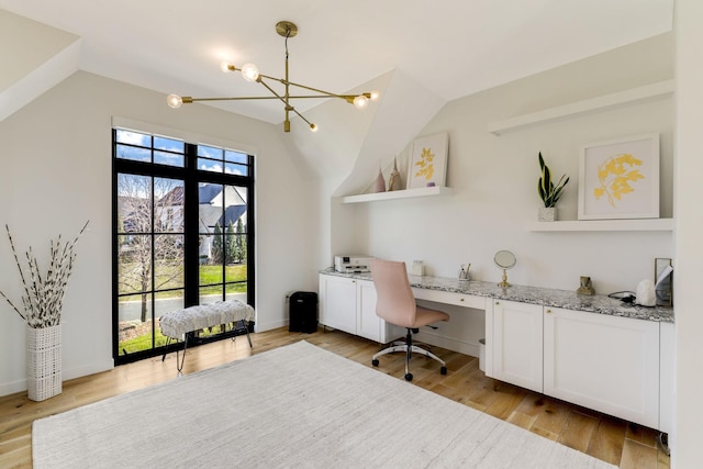 home office featuring light wood-type flooring, an inviting chandelier, built in desk, and lofted ceiling