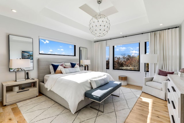 bedroom with light wood-type flooring, a raised ceiling, and a notable chandelier