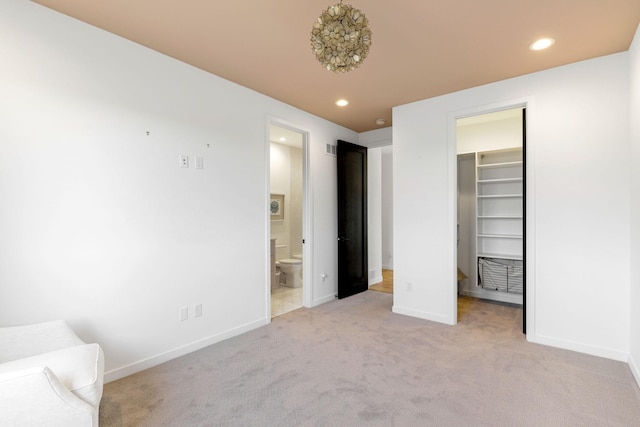 unfurnished bedroom with connected bathroom, light carpet, a closet, and a walk in closet