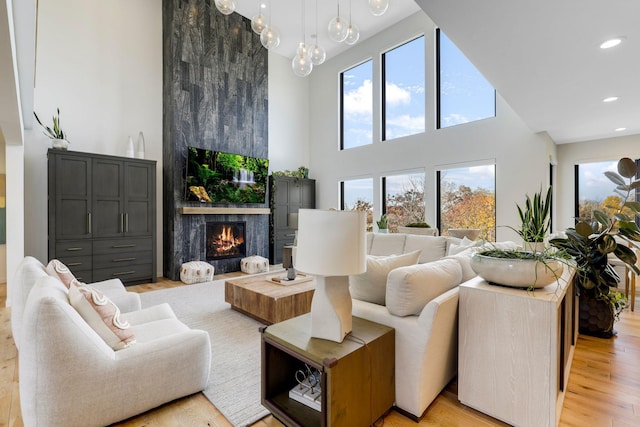 living room featuring a high ceiling, a large fireplace, a notable chandelier, and light wood-type flooring