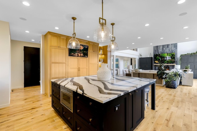 kitchen with decorative light fixtures, a center island, light hardwood / wood-style flooring, light stone countertops, and built in microwave