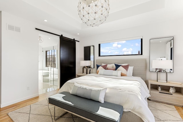 bedroom featuring a chandelier, a tray ceiling, a barn door, and light wood-type flooring