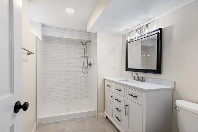 bathroom with vanity, toilet, a textured ceiling, and tiled shower