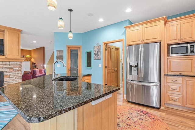 kitchen featuring sink, light brown cabinets, pendant lighting, dark stone counters, and appliances with stainless steel finishes